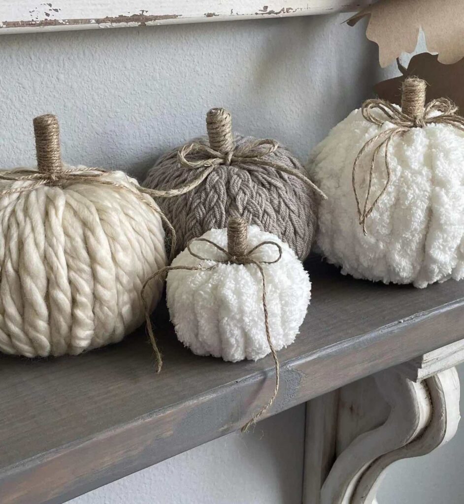 Four decor pumpkins on a ledge all made from different yarns with stick stems