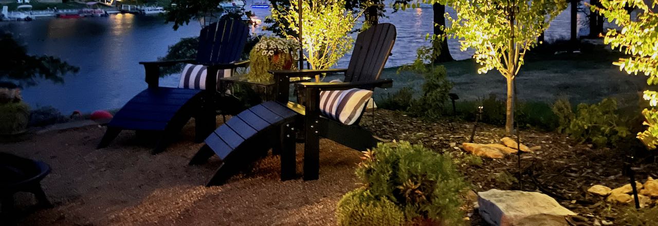 wide image of three trees up lit next to a patio