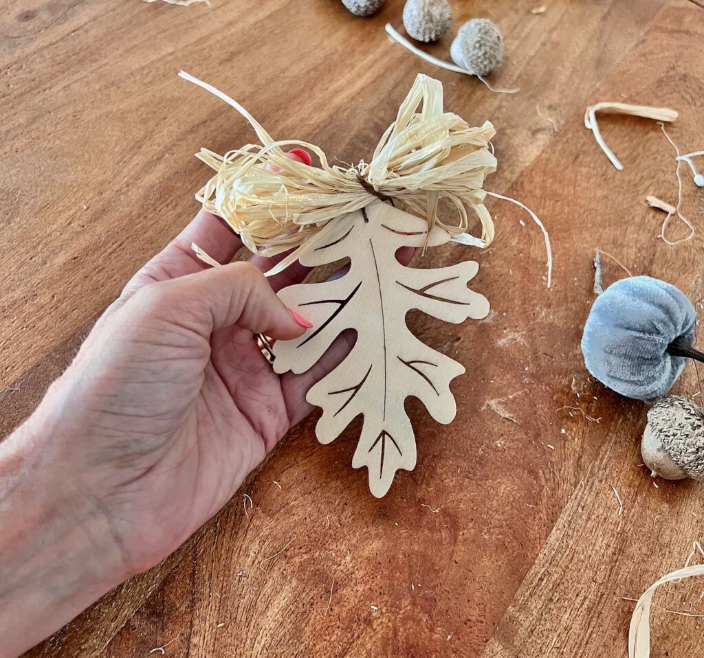 Hand holding one wood leaf with a small bundle of raffia wired on the stem in a bow shape