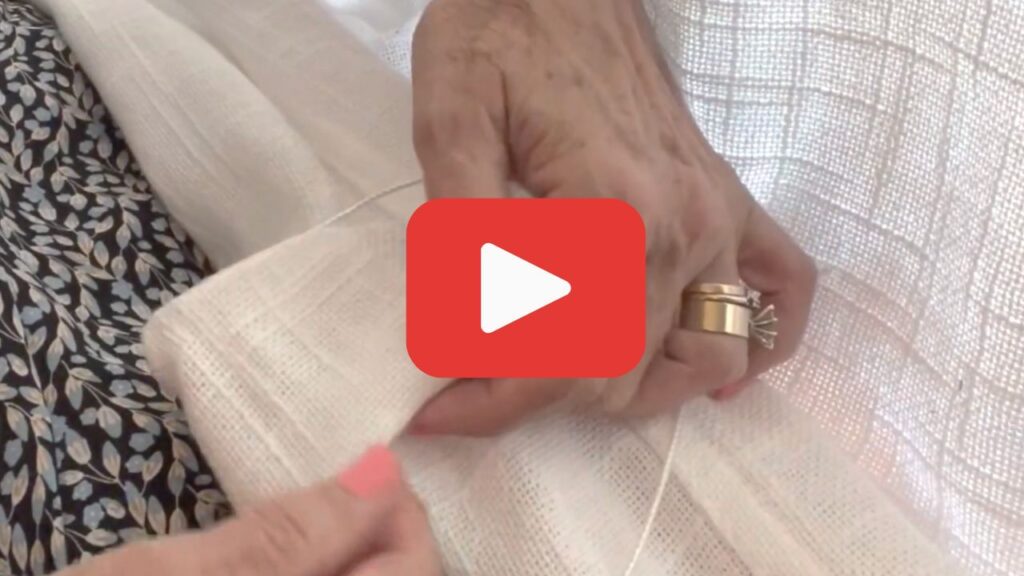 A video play button is shown over a closeup of a woman's hands working on the backside of a Roman shade