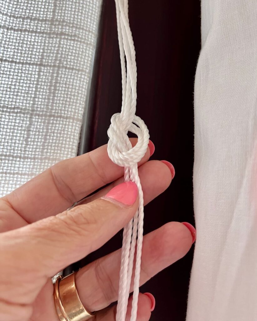 Closeup of a woman's hand hold a bundle of four drapery cords of a Roman shade that are tied in a slip knot