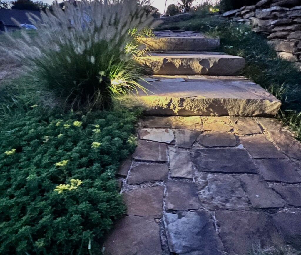 three stone pathway steps are lit with lights in the landscaping