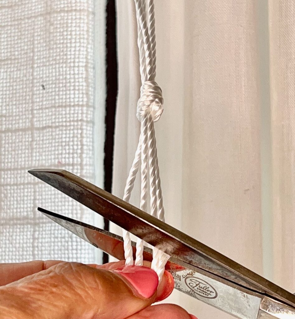 closeup of scissors cutting off the excess of a bundle of four drapery cords tied in a slipknot