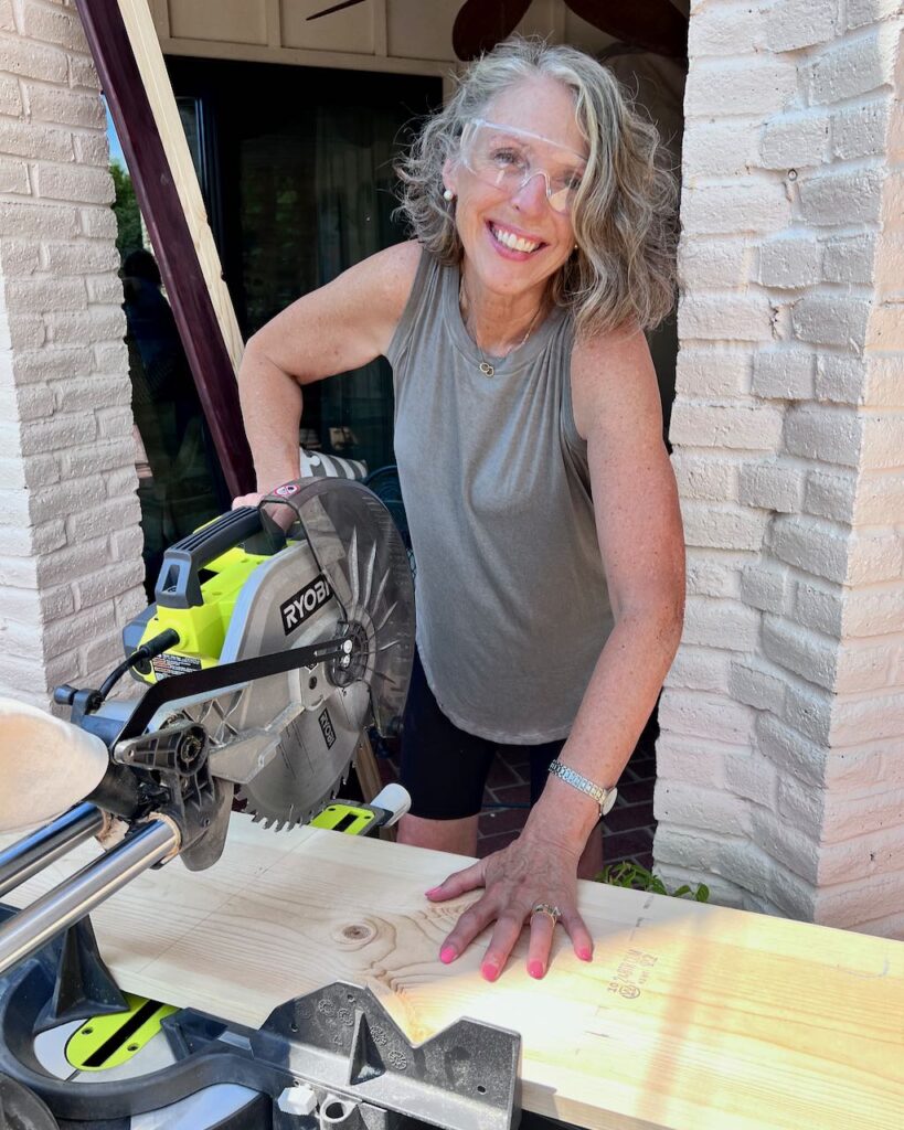 smiling woman wearing safety glasses cutting a wide shelf with a sliding miter saw