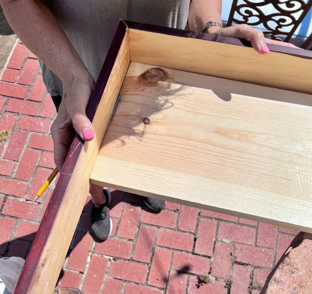 woman's hands holding two pieces of wood forming a mitered corner around the shelf