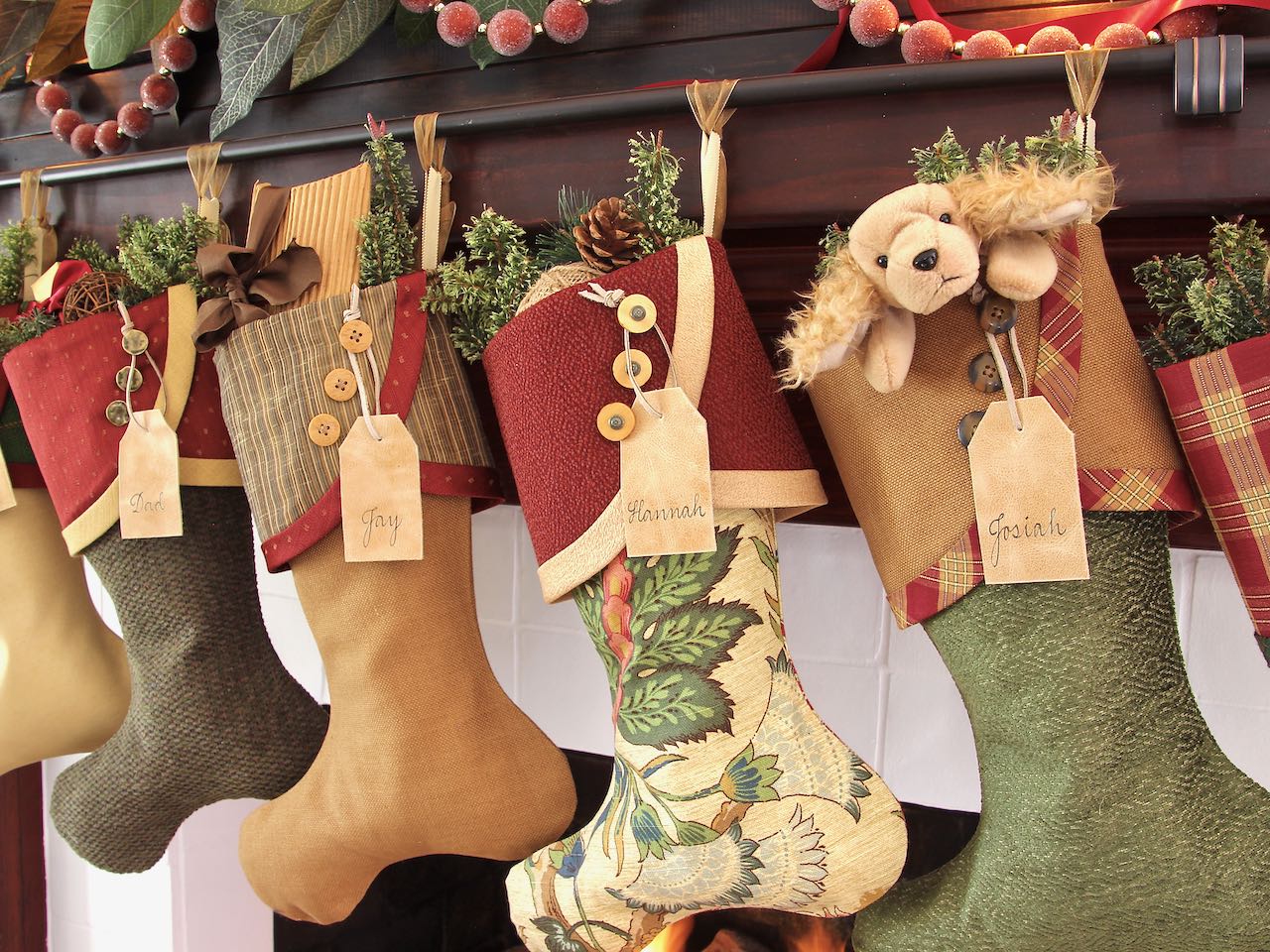 4 coordinating Christmas stockings are hanging with tan leather name tags hanging from their buttons