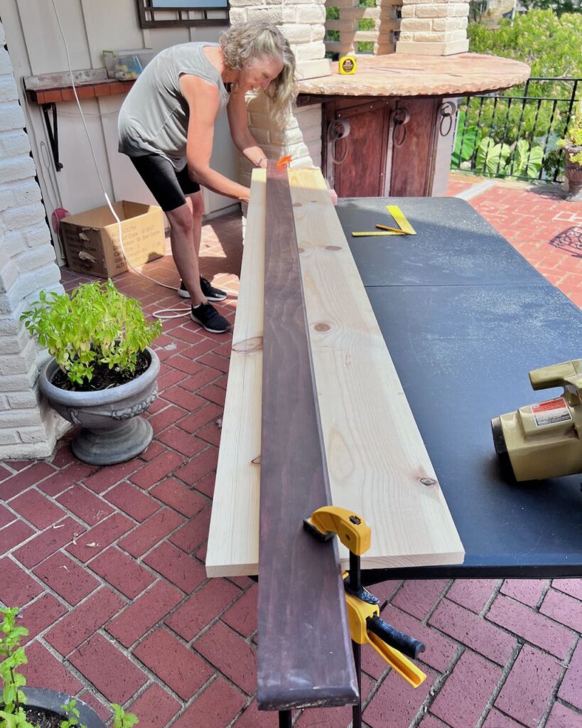 Woman in distance attaching a long piece off wood to a table to cut it