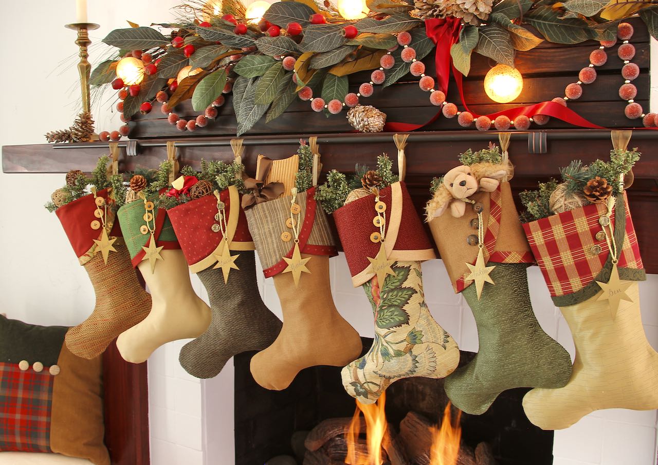 Festive Christmas Stockings are hanging from a dark mantel with green and garland above