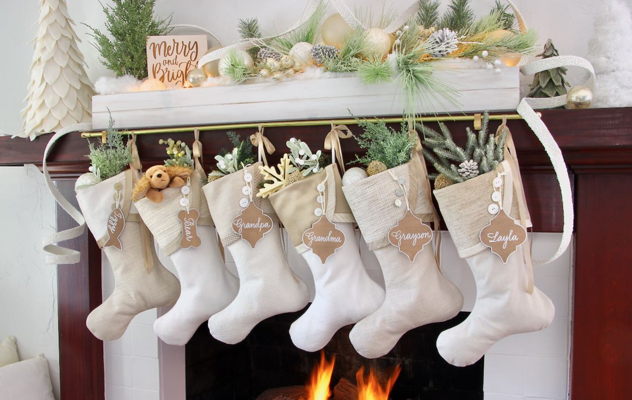 Six unique, butt coordinating white Christmas Stockings with arabesque shaped name tags hang from a decorated mantel.