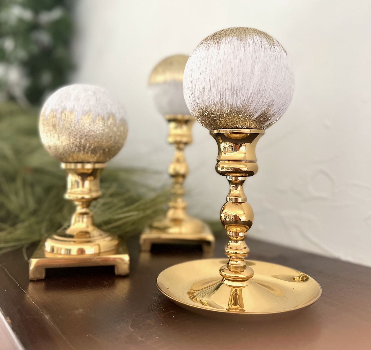 Three Made Over old Christmas ornaments on brass candlesticks on a dark stained mante;