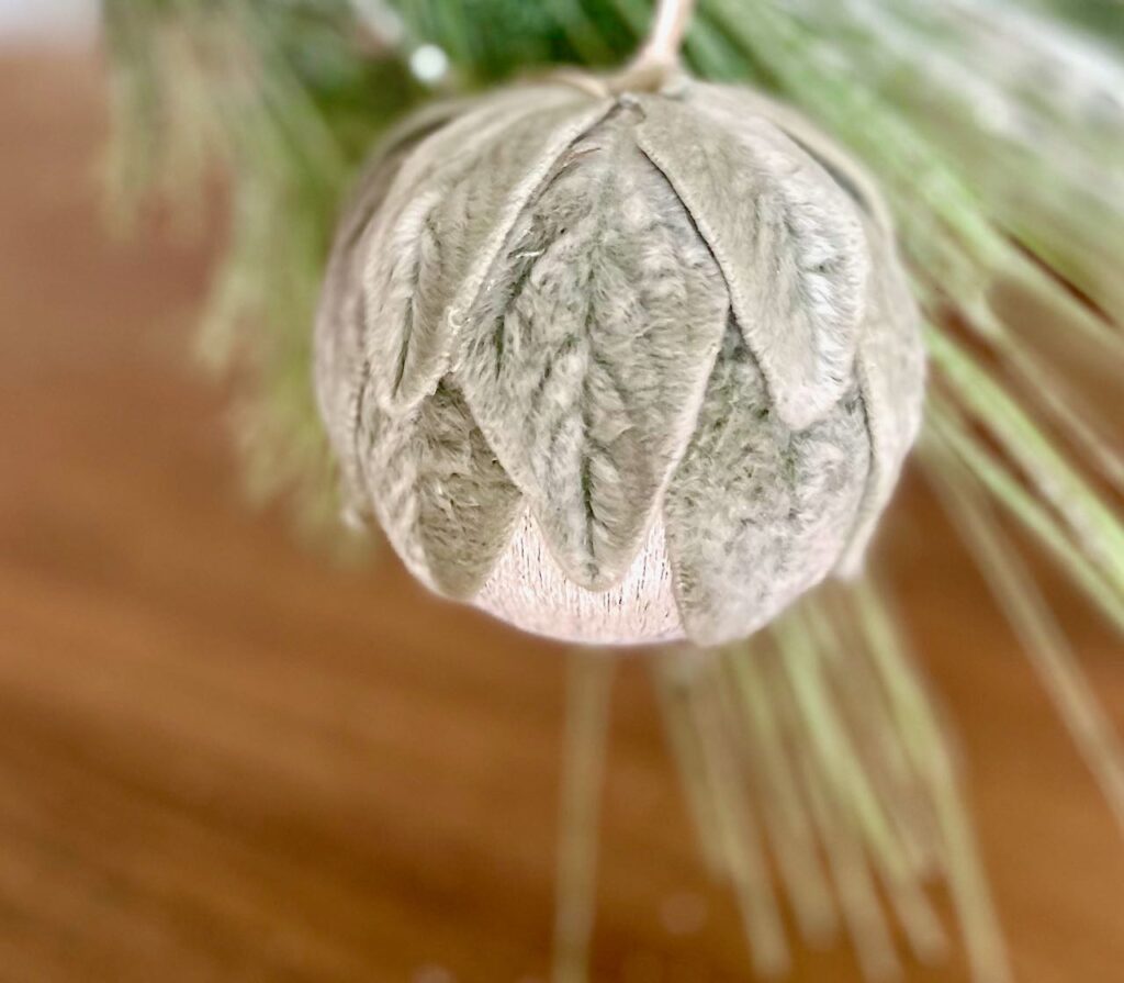 Closeup of a Lambs Ear covered Christmas Ornament hanging from a fir branch
