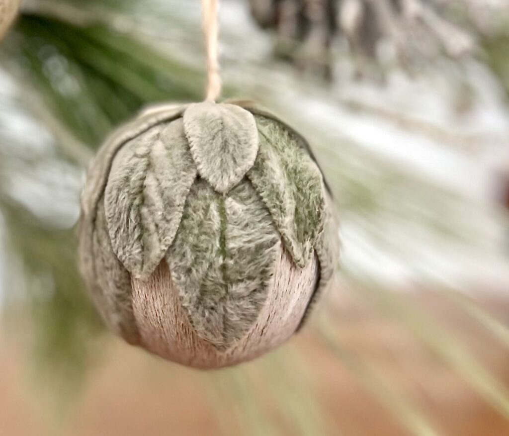 A Lambs Ear Christmas ornament hanging from a fir branch