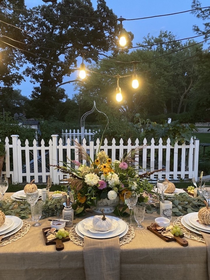 outdoor table setting with fresh flowers, and burlap tablecloth and string light s above