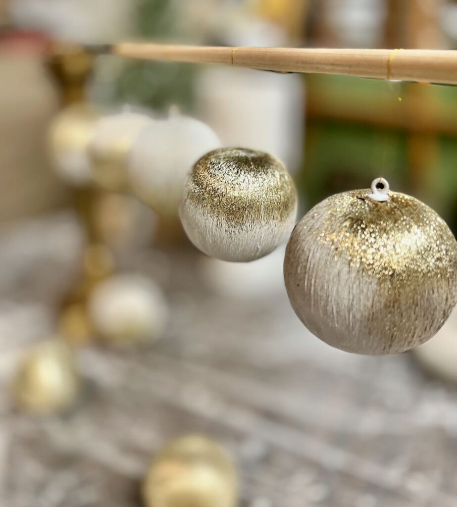 Five freshly painted ornaments hanging from a dowel rod to dry