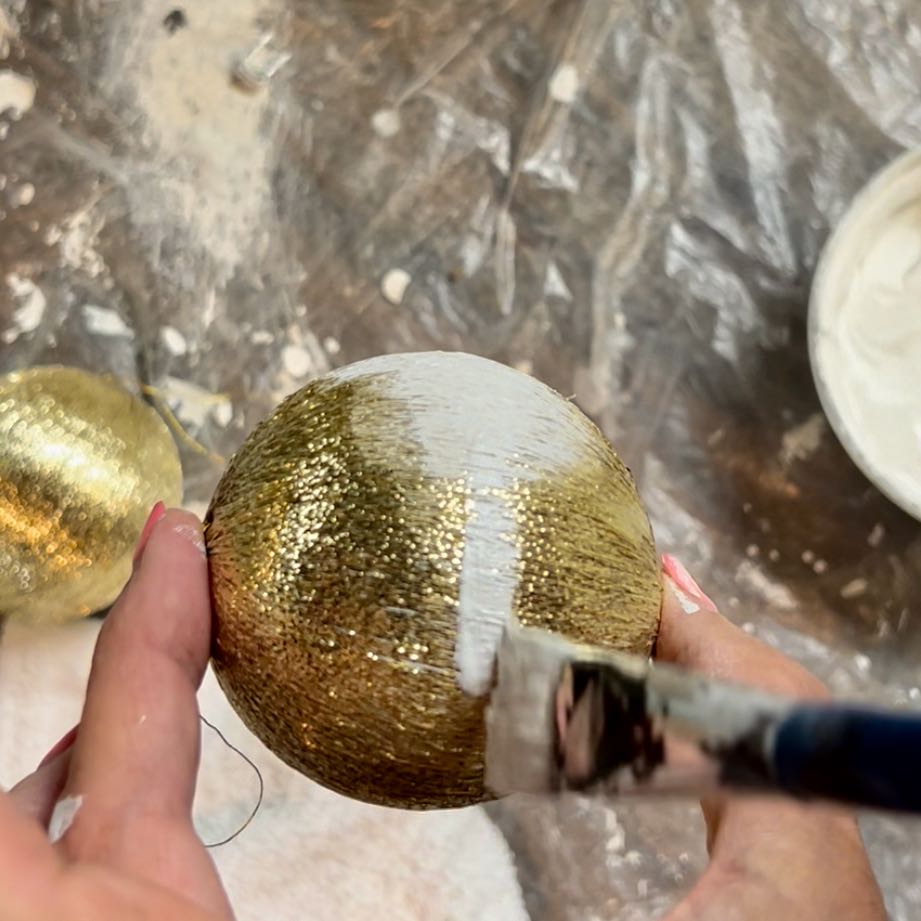 fingertips holding old string wrapped ornament and painting a stripe on it