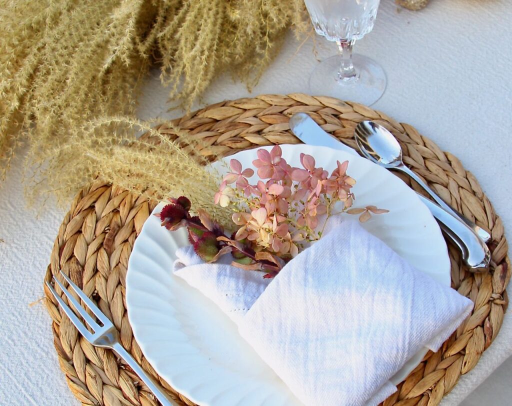 closeup of three foraged plants tucked in a linen napkin on a white plate on a water hyacinth round mat