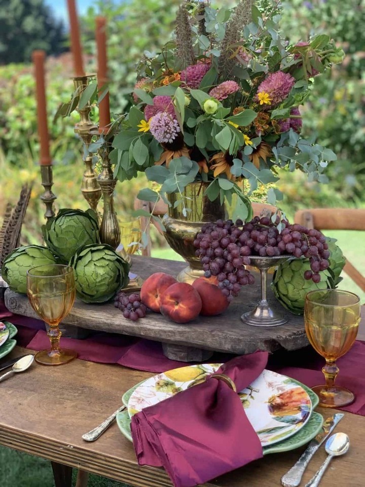 an elegant table with a centerpiece with fresh flowers and fruit on a wood riser