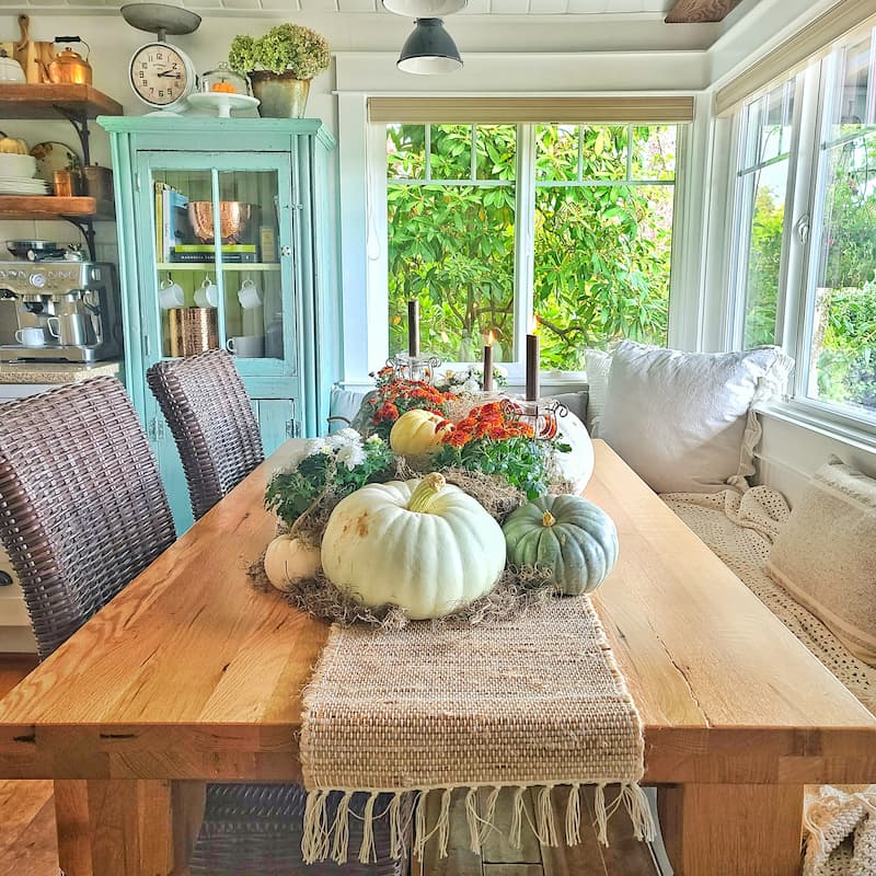 A Fall centerpiece of pumpkins and mums all joined by mounds of dried moss on a thick table runner