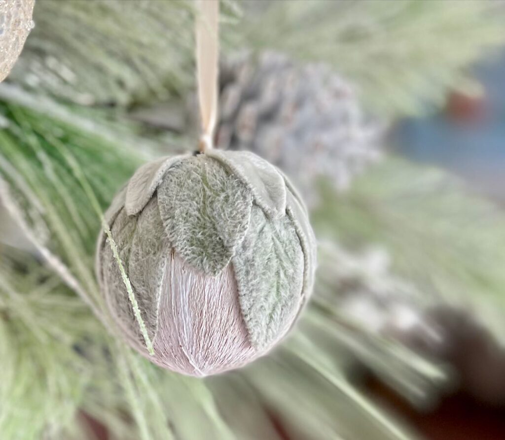 Closeup of a lambs ear ornament hanging with green fir branches behind