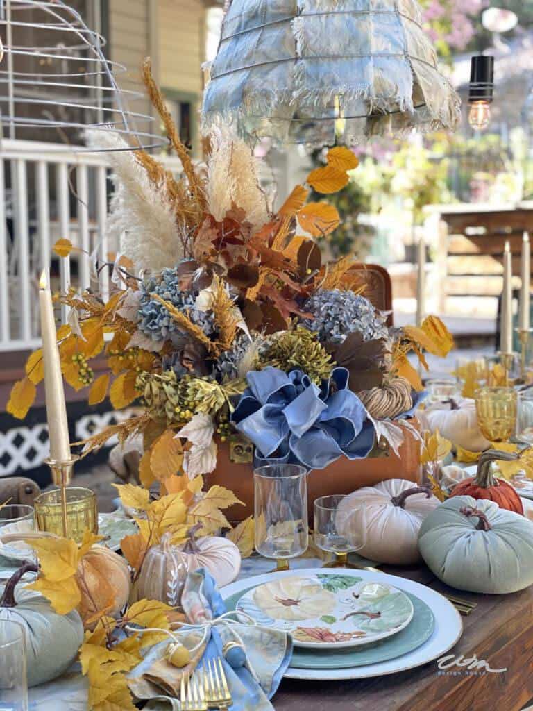 An Outdoor table set with fall leaves and dried grasses in a leather suitcase for a centerpiece