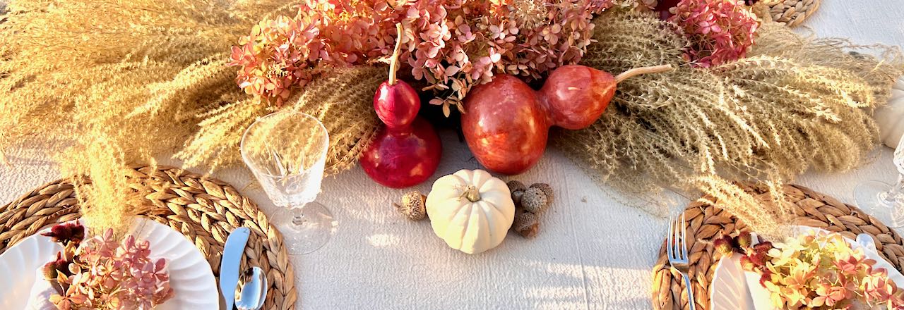 Closeup of two dyed gourds and a pumpkin nestled by a centerpiece of fall grasses and hydrangea blooms