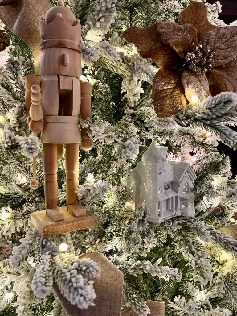 closeup of a nutcracker and ceramic house on a flocked Christmas tree