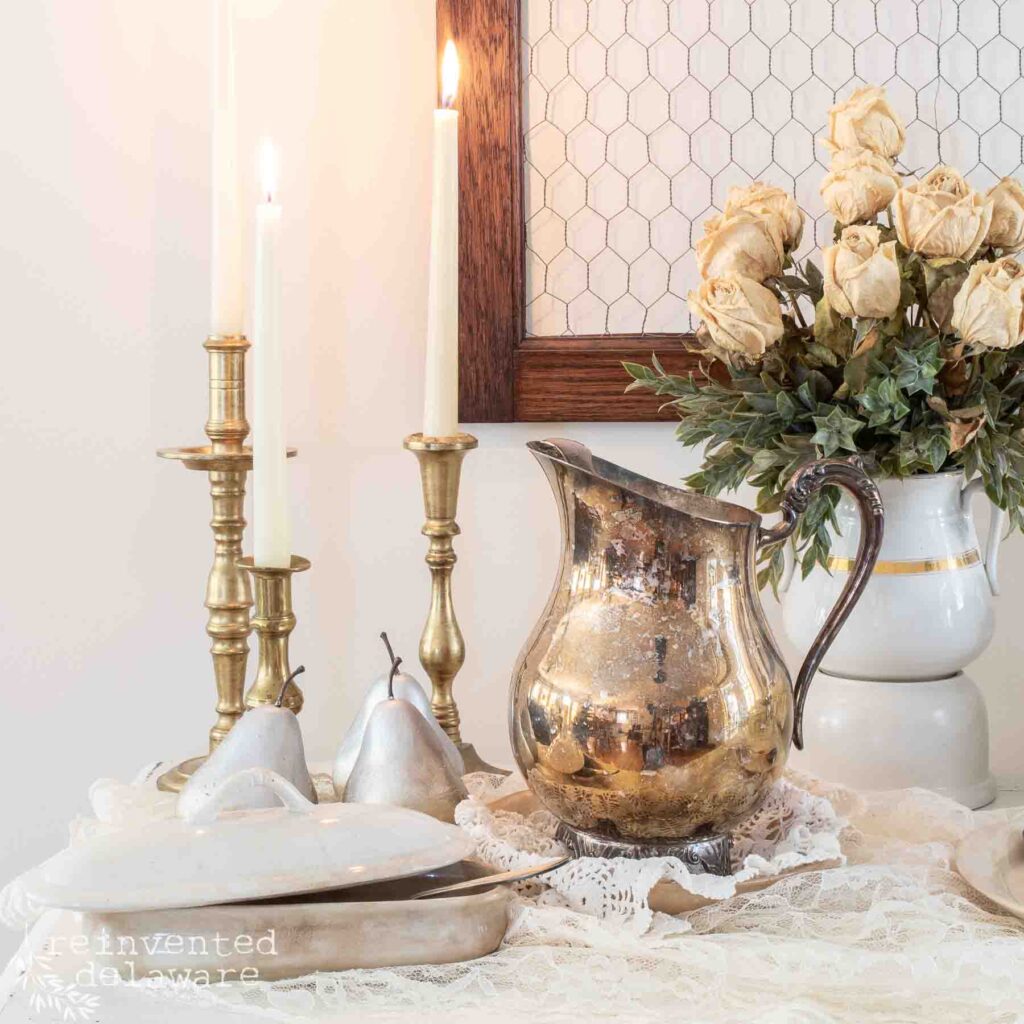 empty vintage frame beside three viintage candlesticks and a pitcher