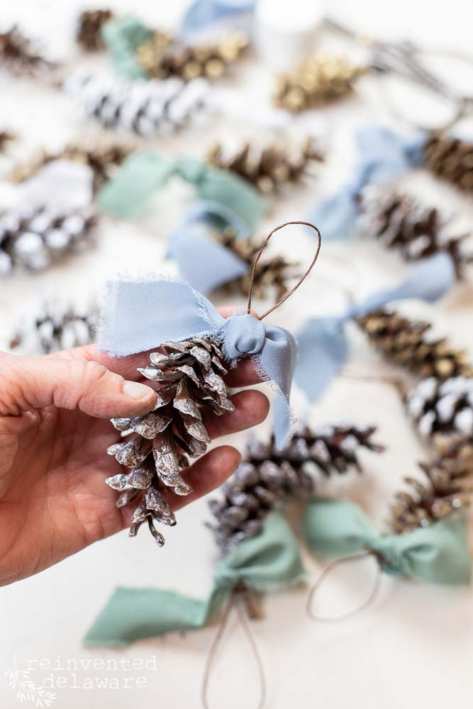 closeup of a hand holding a pinecone ornament with ribbon tied around the hanger