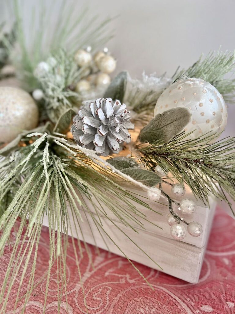 closeup of the end of the wooden centerpiece box with frosted bulbs and branches hanging out