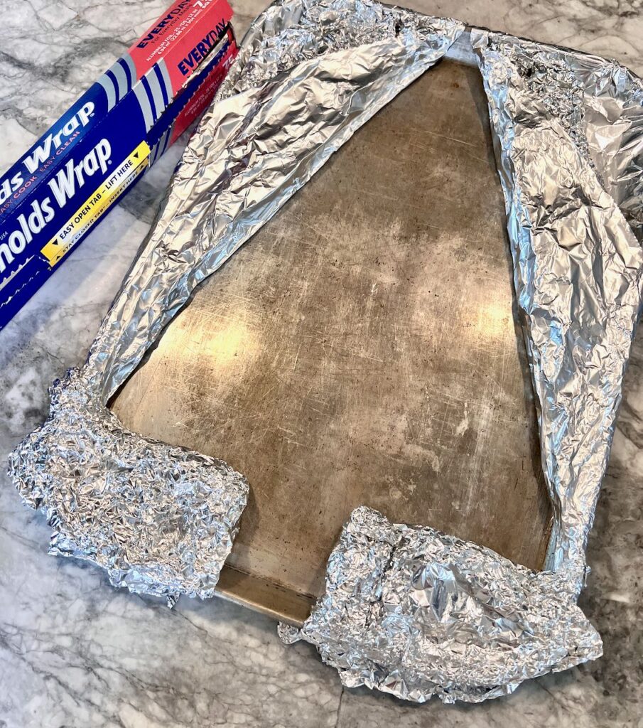 the foil sheets are pulled up and over the triangles and two rectangles creating a void in the cookie sheett shaped like a Christmas tree