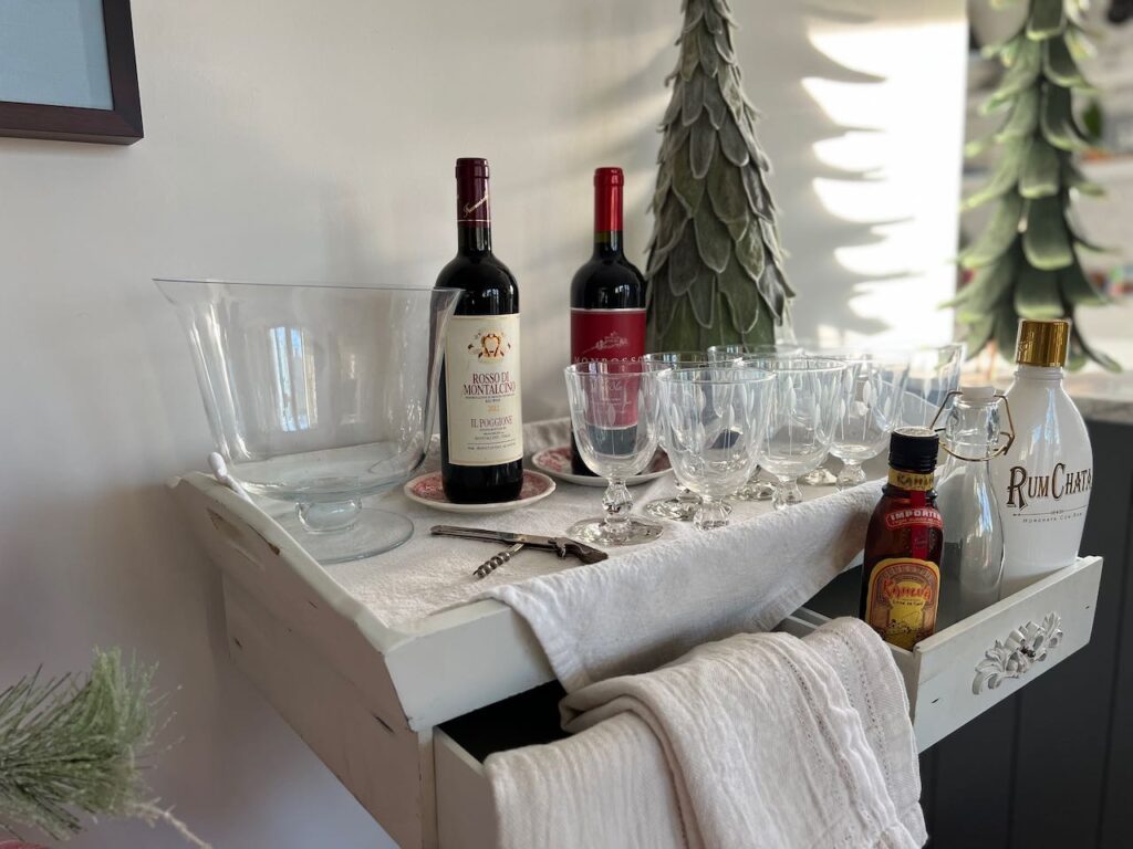 the bar station withh a large glass bowl for ice and white wine next to two red wine bottles with empty wine glasses lined up in front