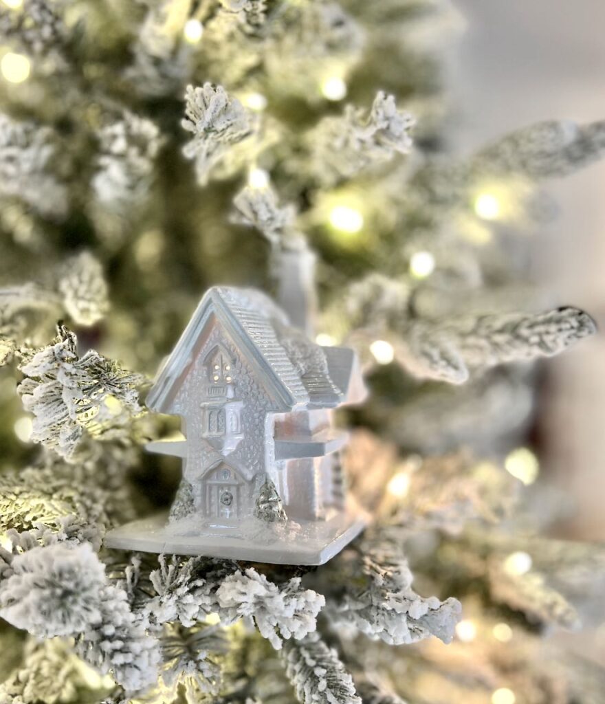 closeup of the detail of a small ceramic house that's lit in side and sitting on some flocked tree branches