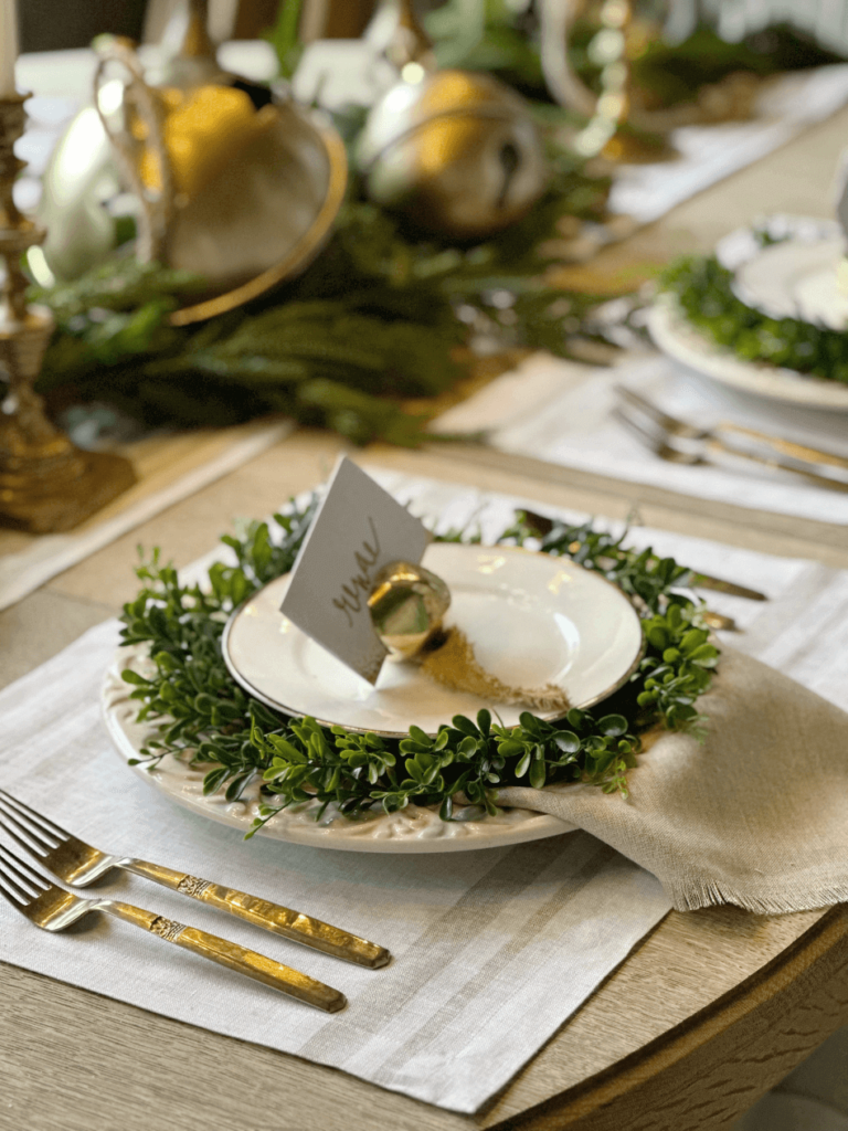 Christmas table setting with greenery and brass bells and candlesticks