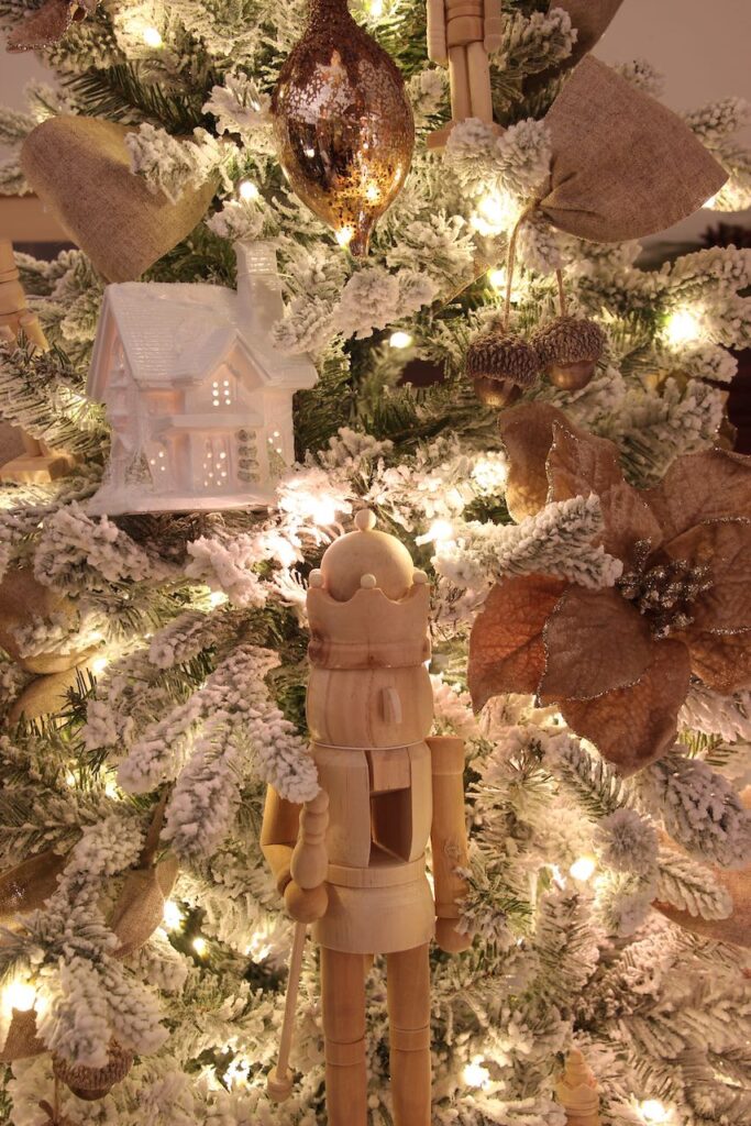 Closeup of a velvet poinsettia, a ceramic house and unfinished wood nutcrackers on a flocked Christmas tree