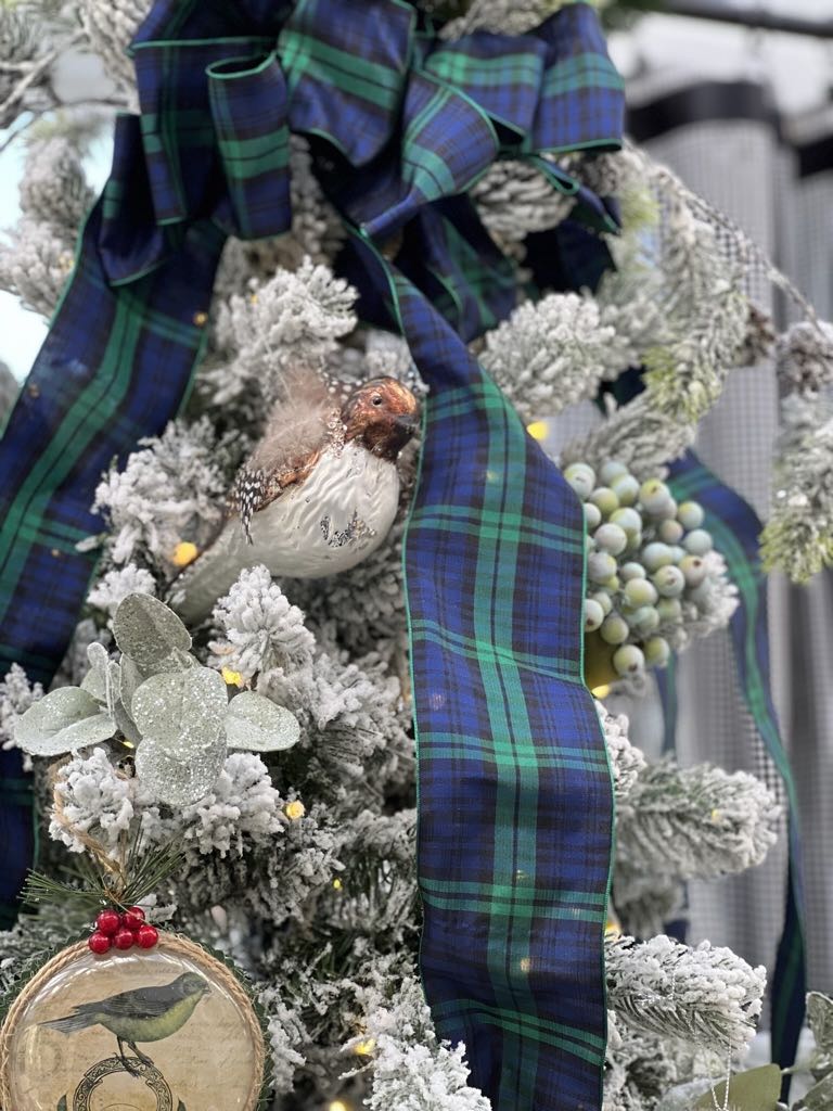 top of a flocked Christmas tree with plaid ribbon and bird images and statues