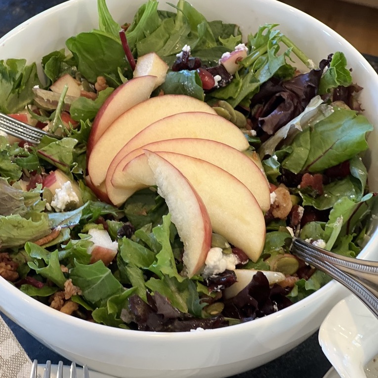 green salad in a bowl with sliced fruit on top