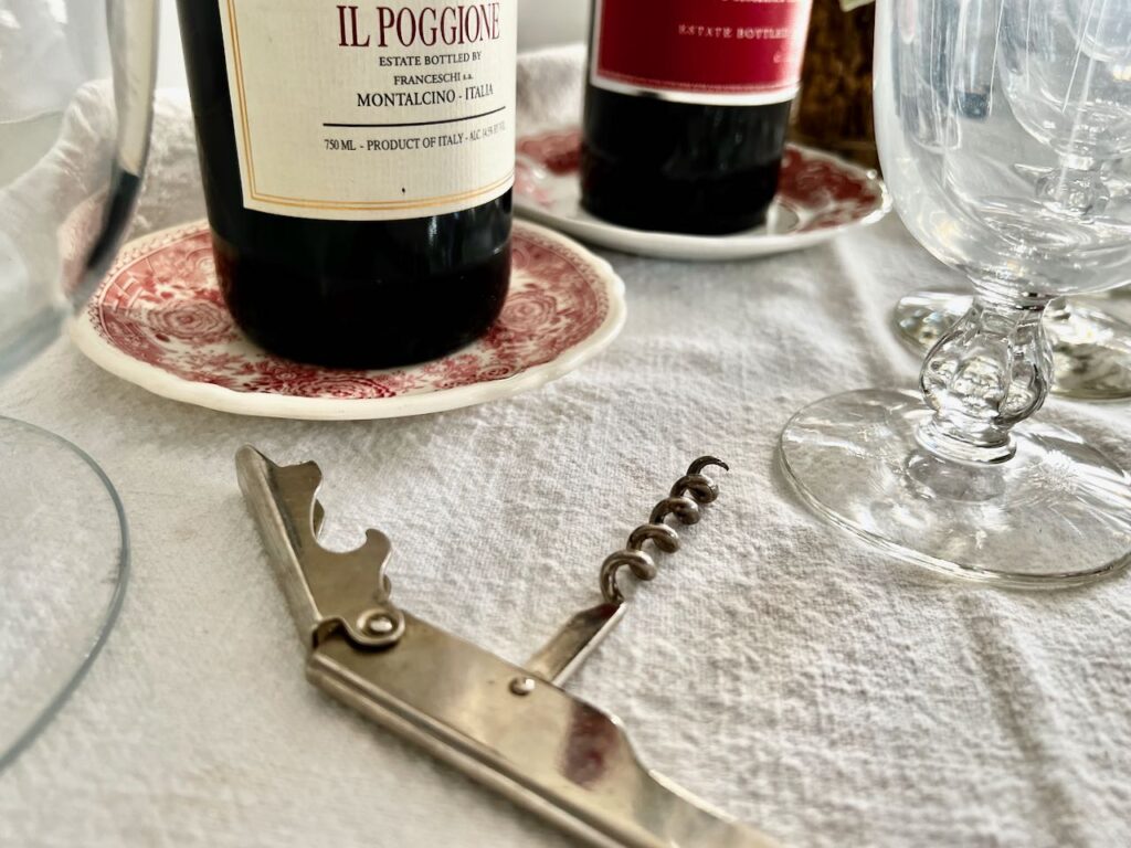 closeup of two red wine bottles on red and white transferware saucers with a wine bottle opener in front
