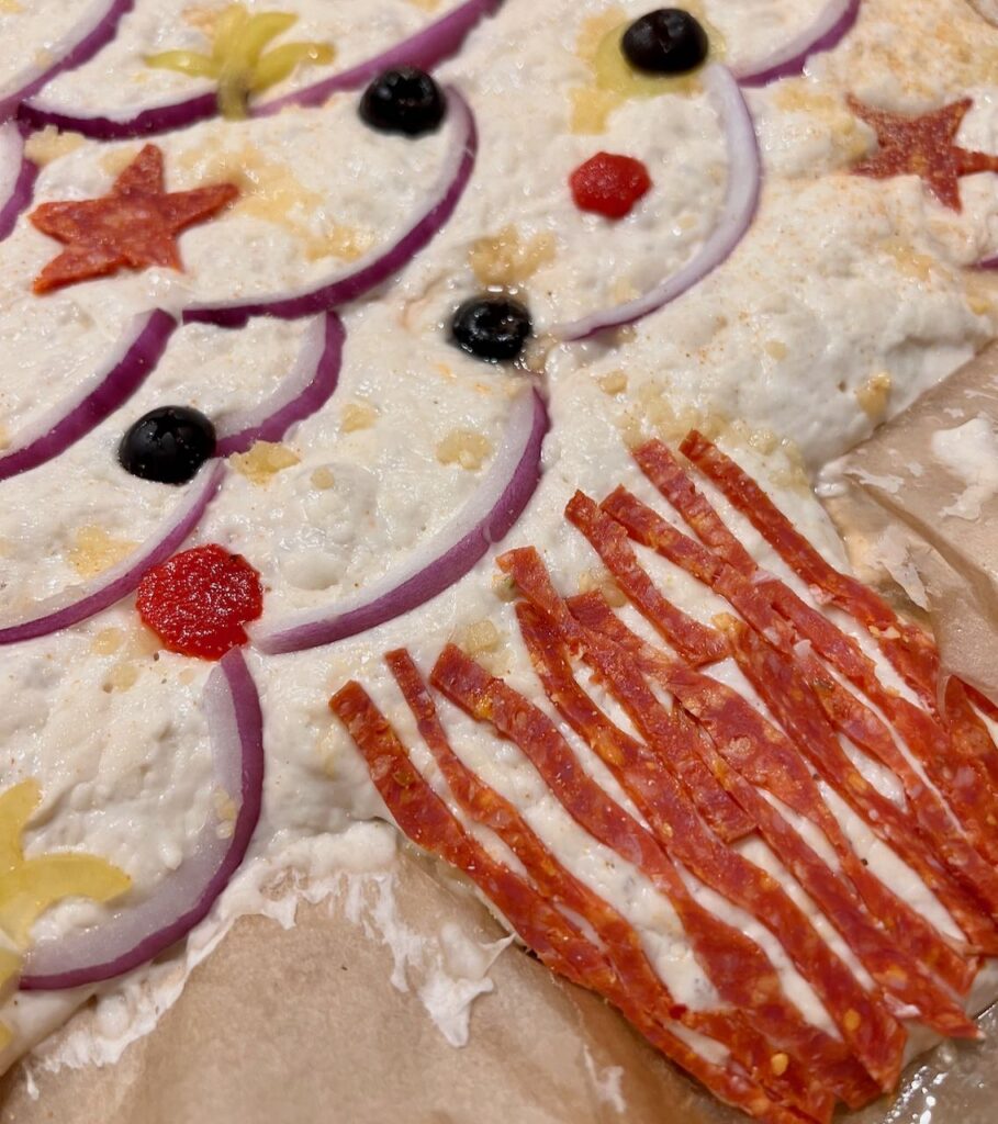 closeup of decorated dough with thin pepperoni slices for trunk bark