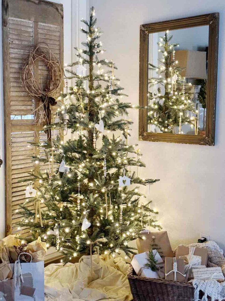 Farmhouse Christmas tree with lights and ornaments with piles of neutral wrapped packages under the tree