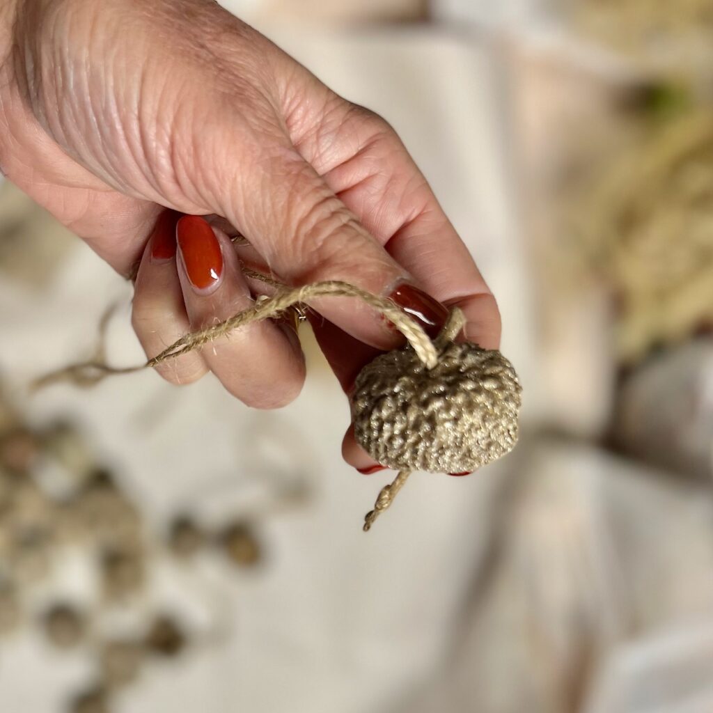 Woman's hand holding the cap of an acorn with twine threaded through a hole drilled in the cap