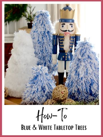 a tray holds a tall nutcracker surrounded by three fluffy blue and white Christmas trees with one white fluffy tree.