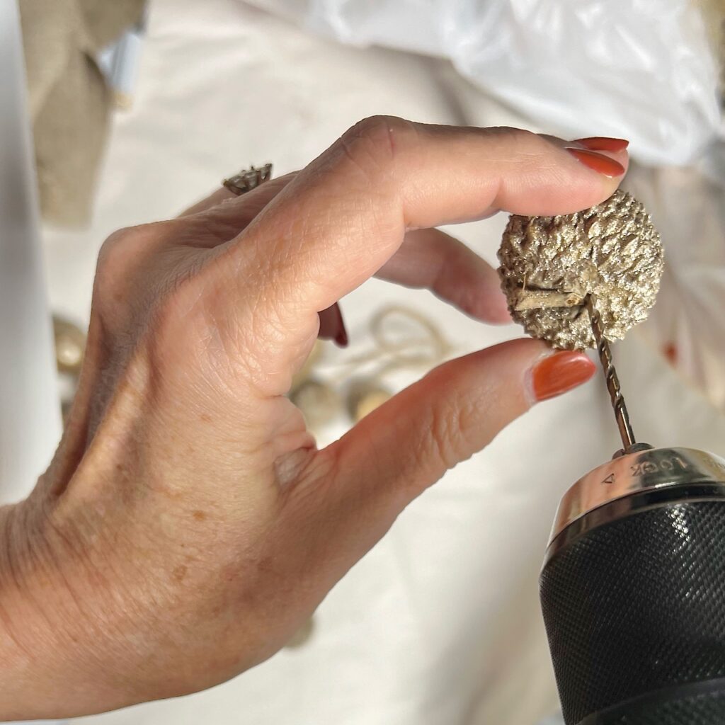 woman's hand holding the painted cap of an acorn with a drill drilling a hole in it