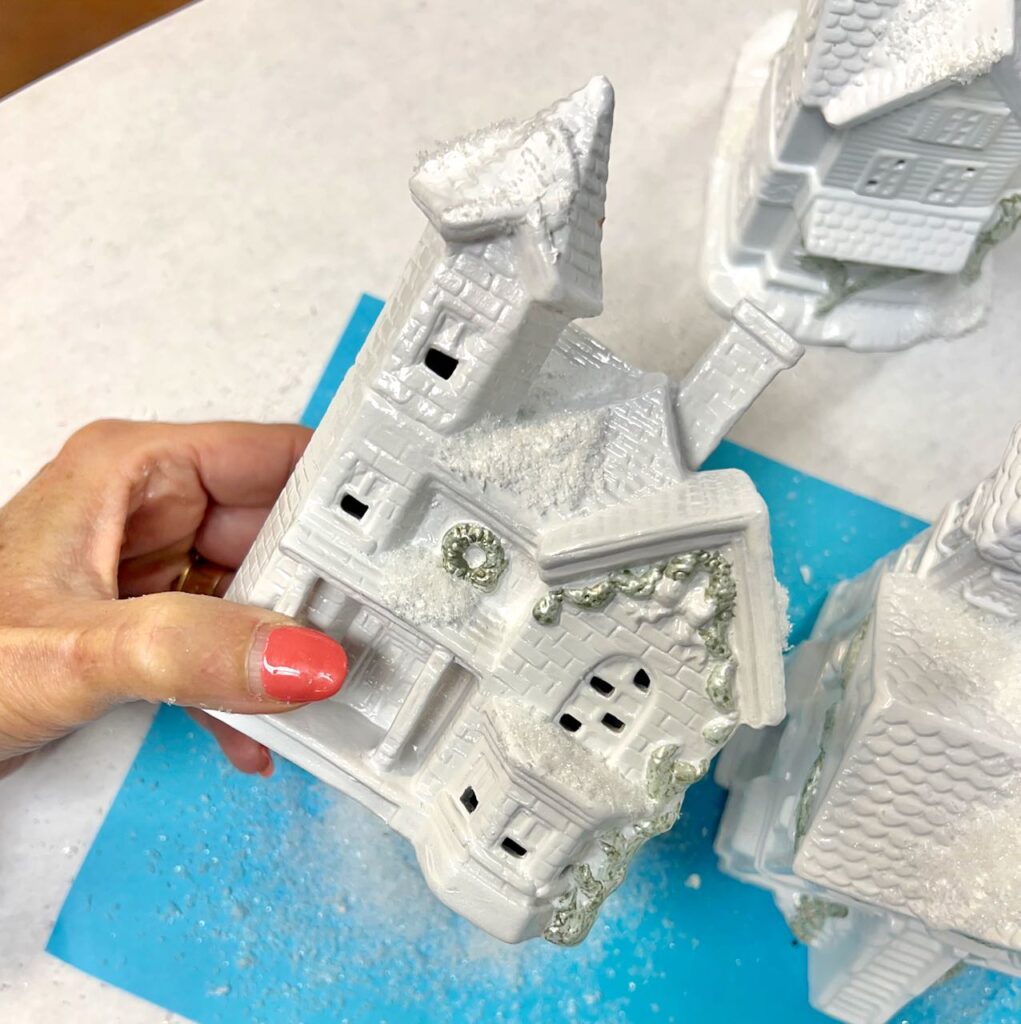 hand holding a house shaking the excess snow off onto a bright piece of paper below