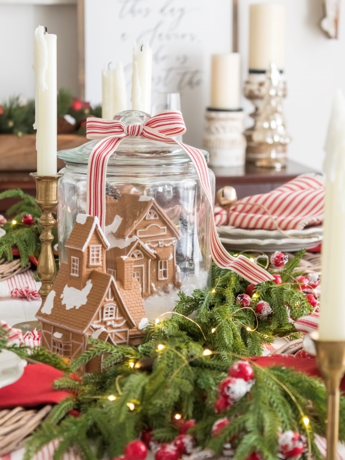 gingerbread house in a gallon glass jar with another gingerbread house as a centerpiece