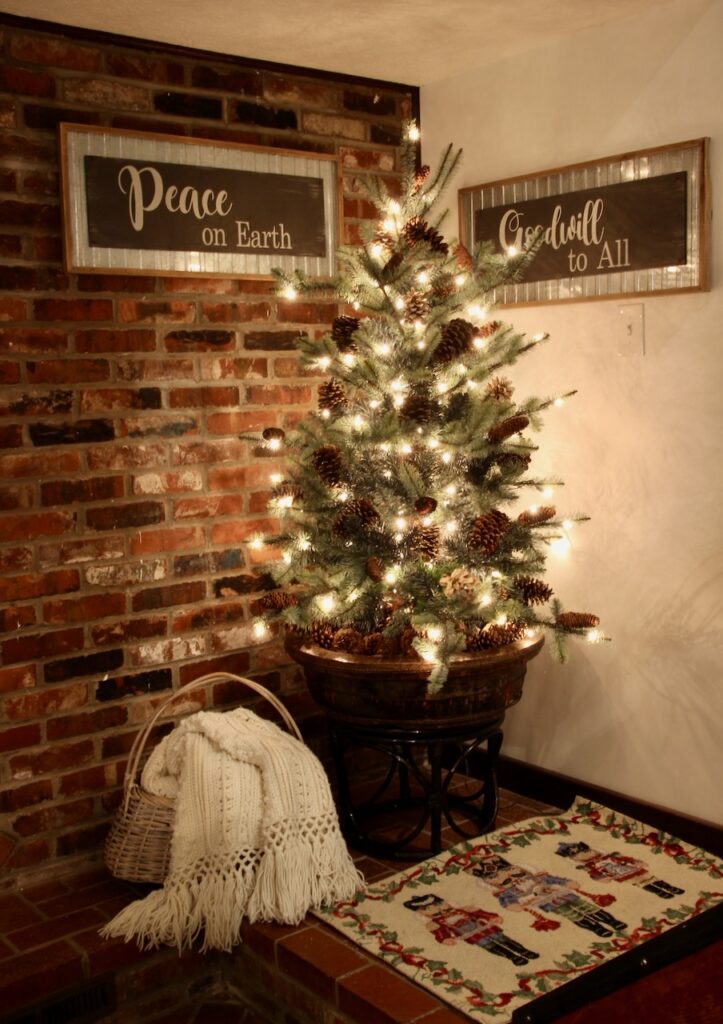 Christmas tree in the corner of a white wall and antique brick wall at the bottom of a flight of stairs