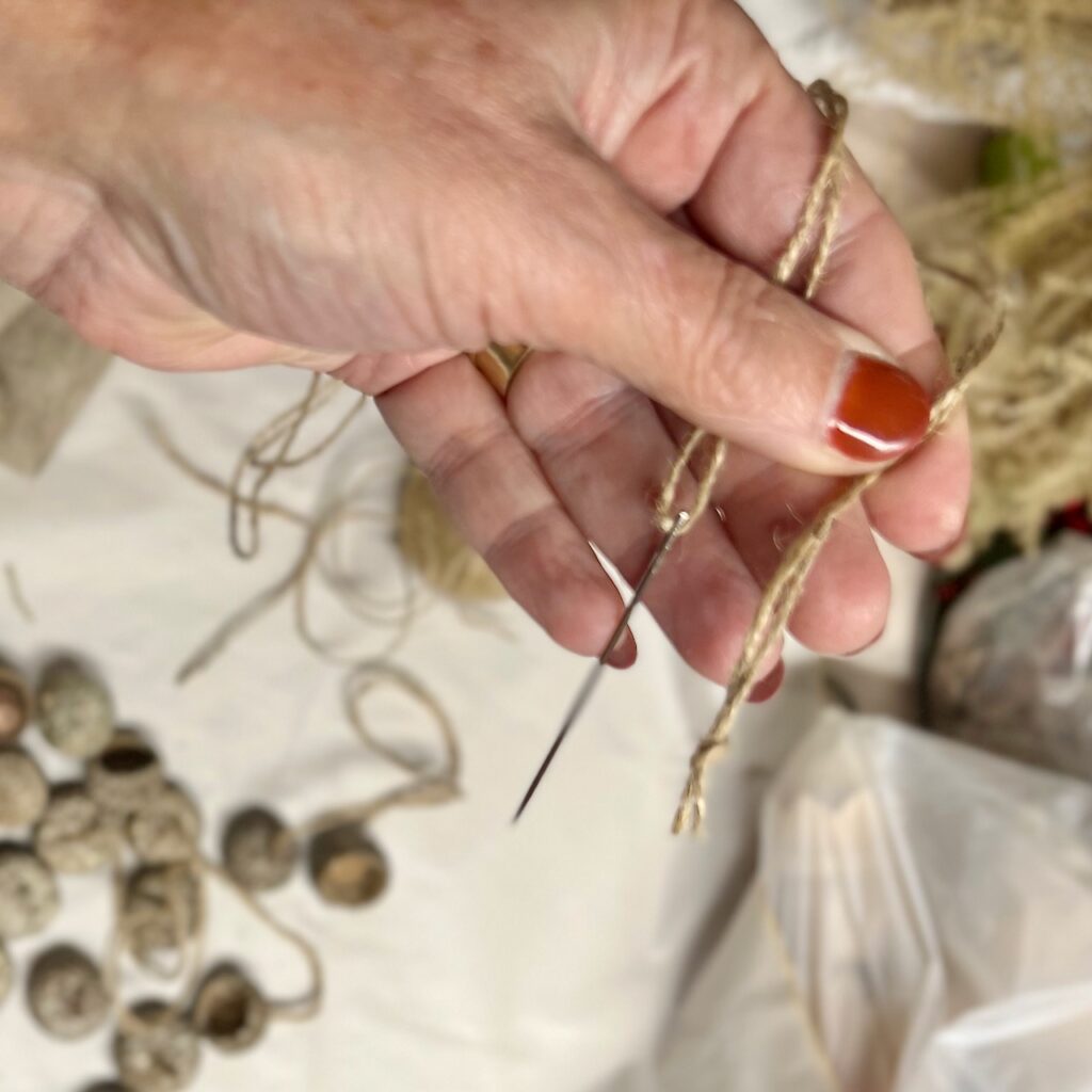 woman's hand holding a needle threaded with jute and the end of the jute is knotted