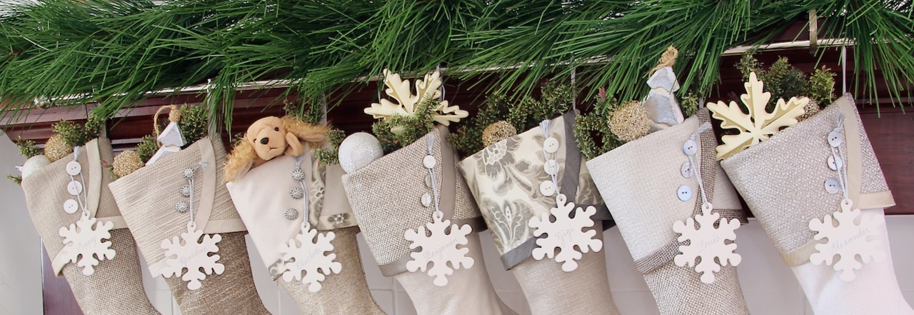 neutral Christmas stockings hanging from a stocking rod partially hidden under greenery