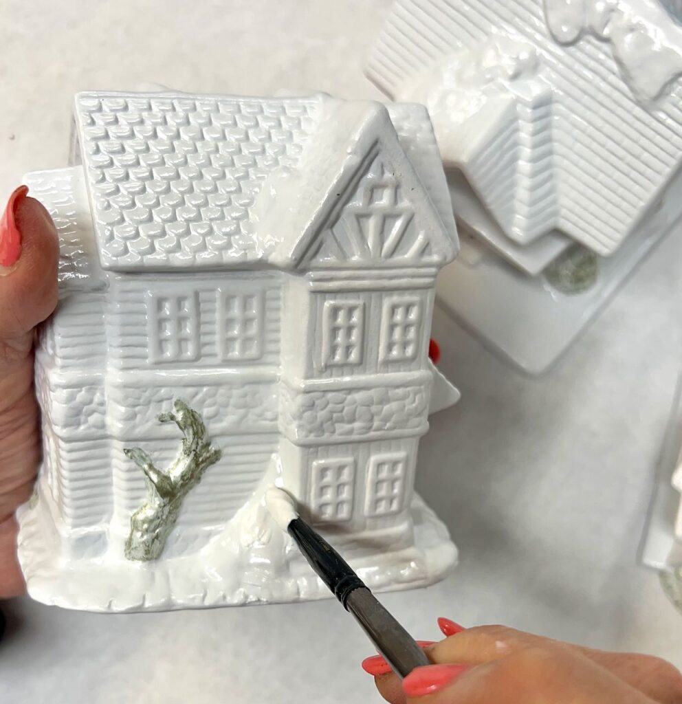hand holding house and paint brush with the white base paint for the snow