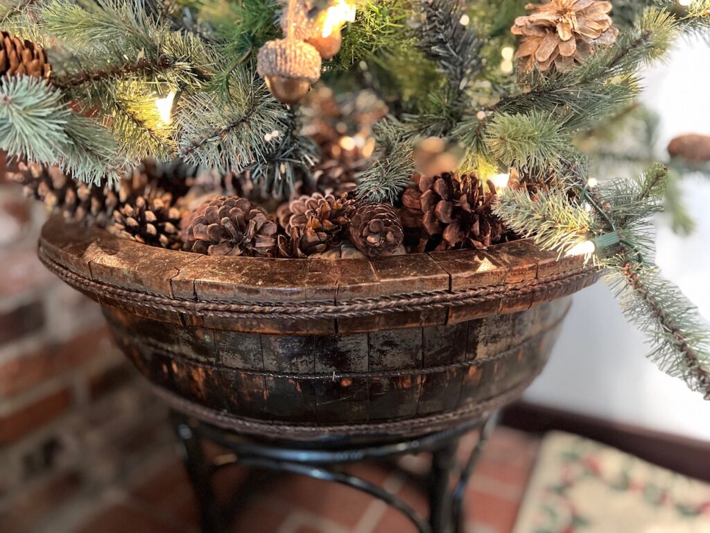 Closeup of a large antique wooden bowl holding a Christmas tree stand buried under s layer of pine cones