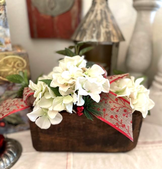 Antique sugar mold is decorated for winter with some white flowers and a large tapestry bow